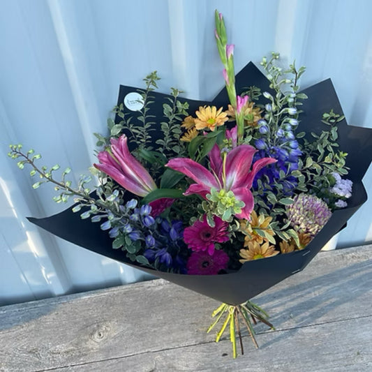 Vibrant Large Seasonal Bouquet with colorful gerberas, lilies, and chrysanthemums, wrapped in brown paper with a matching ribbon.