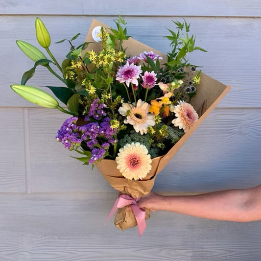 Vibrant medium seasonal bouquet with locally grown lilies and chrysanthemums, wrapped in brown paper with a matching ribbon.