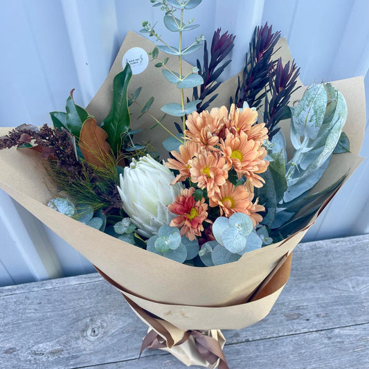 Vibr there, check out this stunning Medium Native Bouquet featuring a bold king protea, vibrant pincushion, and wildflowers, all wrapped in rustic brown paper with a matching ribbon.